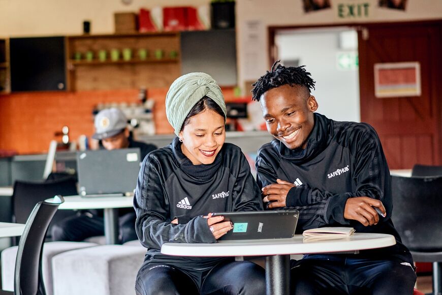 Uma mulher e um homem sentados numa cafetaria a olhar para uma pastilha