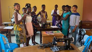 Schoolgirls stand around sewing machines in classroom