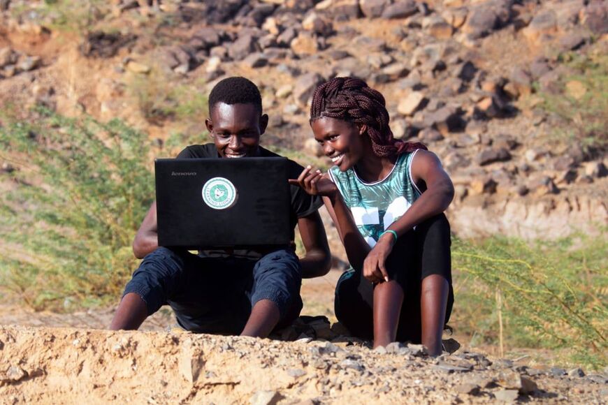 Two students, a woman and a man, sit outside and look into a laptop with a Learning Lions sticker on it